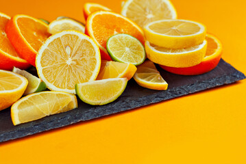 Oranges, lemons and limes cut into slices. Citrus vegetables on an orange background. Preparing vegetables for juice and cocktails. Copy space and free space for text near food.