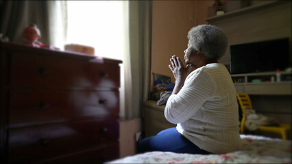 A spiritual older black woman praying to God sitting in bedroom