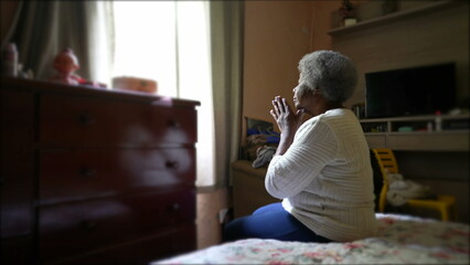 A spiritual older black woman praying to God sitting in bedroom