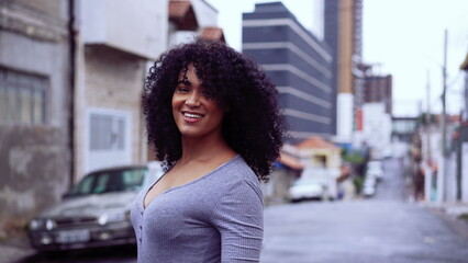 A joyful black woman walking in urban street looking at camera smiling