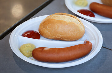 Eine Bockwurst mit Brötchen, Ketchup und Senf auf einem Teller.