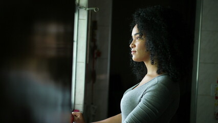 A contemplative young woman standing by window looking outside