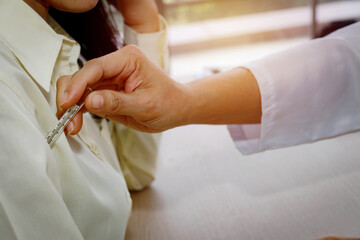 Female doctor's hand examines the body using a mercury thermometer to measure the temperature of a cold patient who is admitted to the hospital.