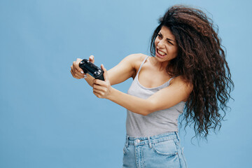 ONLINE GAME AD CONCEPT. Furious beautiful curly Latin lady hold game pad near face, ready to play cool RPG, look at camera. Gaming accessories brands ad. Studio shoot isolated blue background