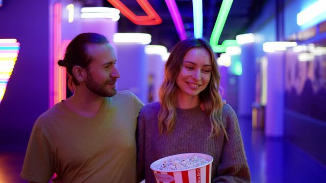 Happy young caucasian woman and man walking by cinema hall, hugging and chatting