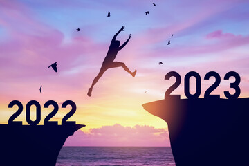 Silhouette man jumping between cliff with number 2022 to 2023 and birds flying at top of mountain. Freedom challenge and travel adventure holiday concept. - obrazy, fototapety, plakaty