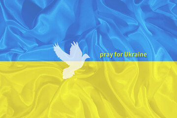 Pray for Ukraine text on the blue and yellow Ukrainian flag with the silhouette of the dove of peace
