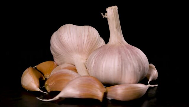 two heads of garlic surrounded by garlic cloves rotate on a black background 