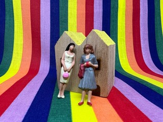 レインボーの背景と家の前に立つ女性同志のカップル。LGBT・同性愛の家族のイメージ。