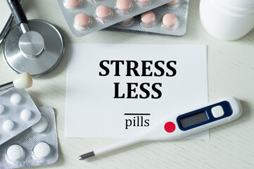 a card with text LESS STRESS on a light table next to a thermometer, stothoscope and pills