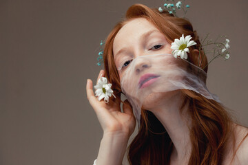 Spring fashion portrait of young woman with chamomile flowers in red hair with white lash. Concept skin eyelash care