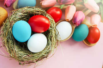 Easter background with colored Easter eggs on pink and spring tulip flowers. Top view with copy space	
