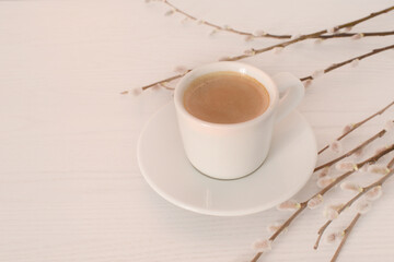 Cup of black coffee and flowering willow branches on a white wooden table. Morning spring coffee