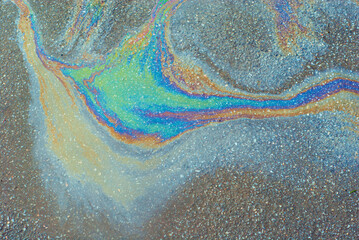 Oil stains on wet asphalt. Puddles are contaminated with multicolored streams of oil. The concept...