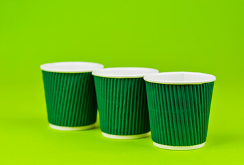 Disposable paper cups on a green background. Ecological coffee utensils. Copy space and free space for text near the glasses.