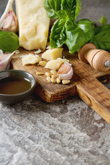 Italian parmesan cheese with knife fresh green basil, olive oil, pine nuts and garlic. Ingredients for the pesto. Dark wood background