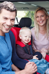 This is a picture for the family album. Portrait of a laughing father and mother next to their toddler who is sitting in his baby seat.