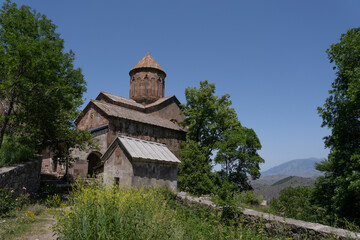 Fototapeta na wymiar a large dark stone church high in the mountains of Georgia, next to which there are green trees and behind it a beautiful blue sky