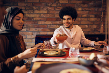 Happy Middle Eastern man having lunch with friends at dining table.