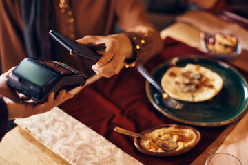 Close-up of woman uses smart phone while paying to waitress in restaurant.