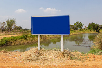 A large, blue, blank sign on the side of the road and the aqueduct.