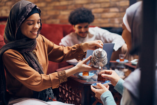 Happy Muslim woman serving Turkish tea to female friend.
