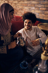Happy Muslim man drinks Turkish tea with is wife while smoking hookah.