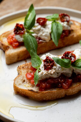 Fototapeta na wymiar Two grilled bruschetta with stracciatella cheese and sun-dried tomatoes on black plate stand, top view, menu photography