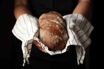 Freshly baked hot bread in hands on a black background. Traditional bakery.