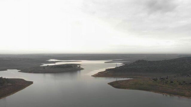Aerial images showing the banks of a reservoir from 100 meters high. Flying over the water, approaching the shore with the sunset in the background. cloudy day with rain clouds