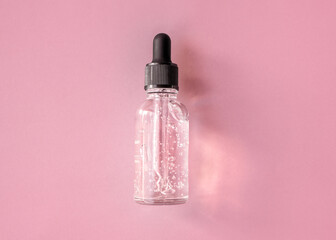Transparent glass dropper bottle with air bubbles on pink background in sunlight. Pipette with...