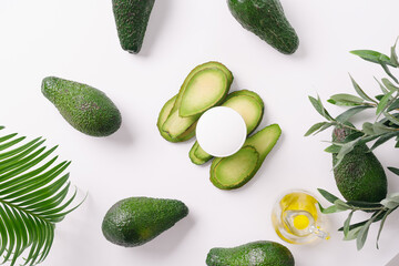 Spa. Photo of cosmetics. White cosmetic container on avocado slices. Among whole avocados. Avocado oil on a white background