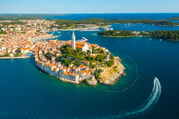 Surroundings of Rovinj and tower of St. Euphemia church. Croatian town buildings near forests and Adrianic sea at bright sunlight. Aerial panorama - obrazy, fototapety, plakaty