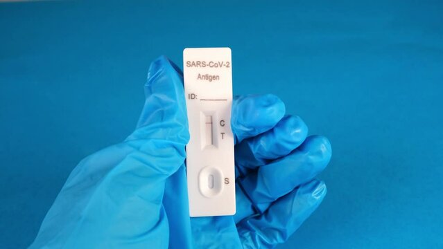 hand in a protective medical glove holds a Negative SARS-CoV-2 Rapid Antigen Test on a blue background