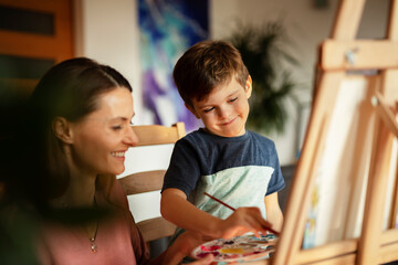 Mother and son painting at home. Little boy drawing with mom in living room
