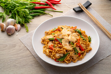 Spicy stir fried instant noodle with sliced chicken breast and thai basil leaves in white plate
