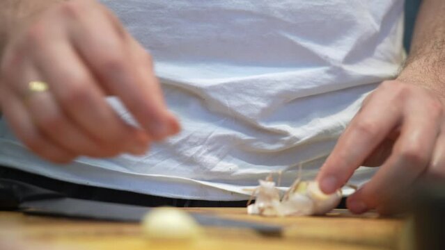 Hands of man in white t-shirt separating cloves of garlic on cutting board. man peels garlic standing at kitchen