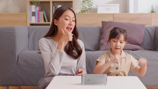 Happy asian mother and daughter sing a song and dancing together watching music video apps in smartphone.Cheerful mom and kid recording video clib and sharing on social media streaming app having fun