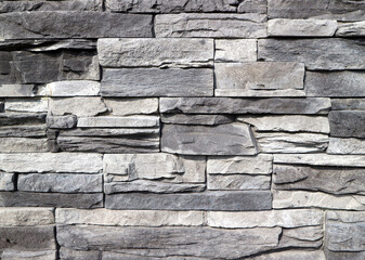 Cladding wall made of  stacked  rough natural stones. Colors are shades of gray. Background and texture.