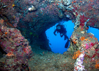 Naklejka na ściany i meble Scuba diver observes a underwater cave in the sea.