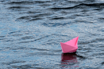 A paper boat, handmade, pink, red, floats in a spring puddle, water. The concept of the change of seasons.