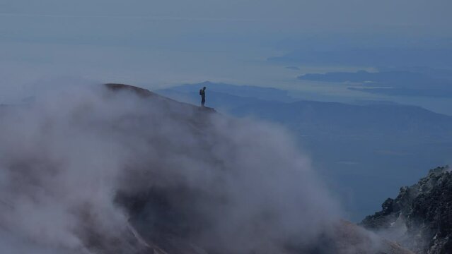 Silhouette of man hiking at coldera of Avachinsky stratovolcano, also known as Avacha Volcano. Backpacker tourist moves upon rocks behind steam from hot geysers. Kamchatka Peninsula, Russia.