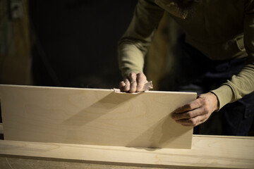 Carpenter grinds board. Man creates furniture. Hands hold sanding paper.