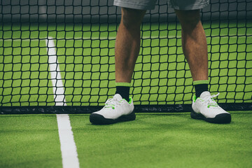 Closeup view of male legs with shorts in a padel tennis court standing near the net. Young athlete ready to start the match. No face Sport, health, youth and leisure concept. White lines in background