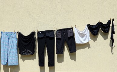 Dark clothes hanging out to dry on a clothesline, by side a white wall.