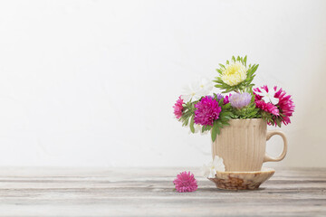 beautiful flowers in cup on wooden table on background white wall