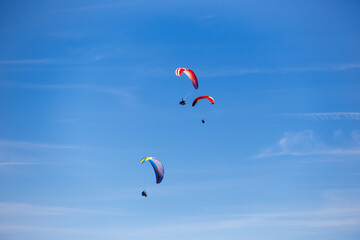 Three paragliders in a sunny blue sky