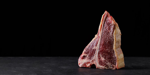 Raw beef steak, dry aged T bone on black background. Free space for text