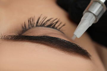 Young woman undergoing procedure of permanent eyebrow makeup in salon, closeup