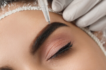 Young woman undergoing procedure of permanent eyebrow makeup in salon, closeup - obrazy, fototapety, plakaty